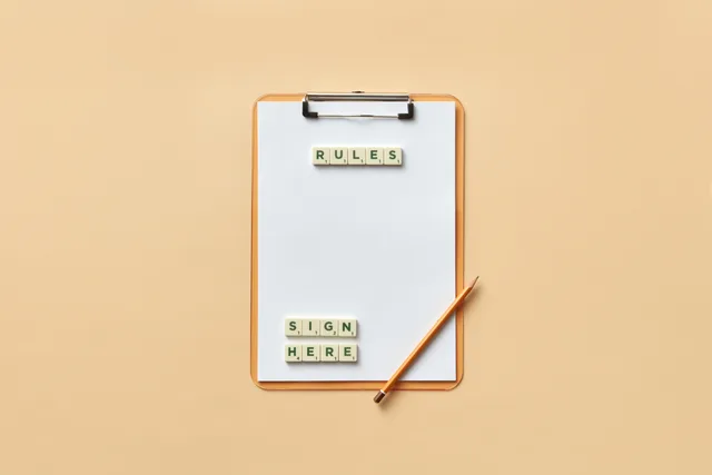 Flat lay of clipboard with letter tiles spelling 'rules' and 'sign here', accompanied by pencil on beige background. Copy til danske kampagner: sprog, regler og læsbarhed